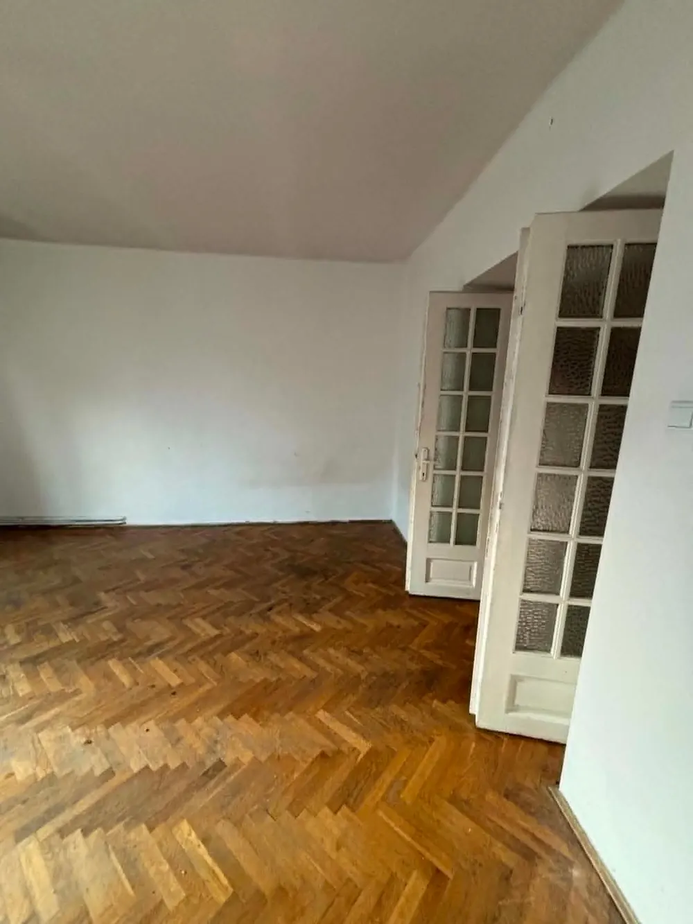 Pusty pokój z parkietem i przeszklonymi drzwiami po opróżnieniu